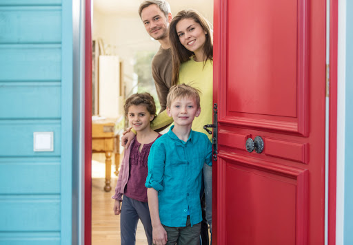 A family of four smiling as they open the front door of a home.