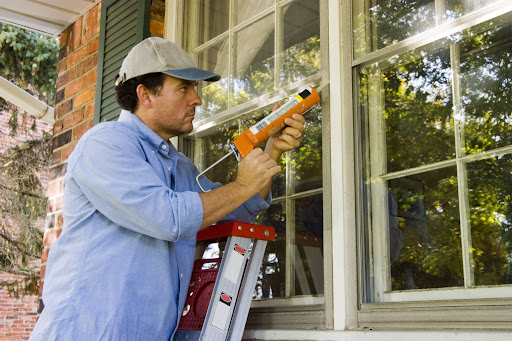 A man sealing a window from the outside.