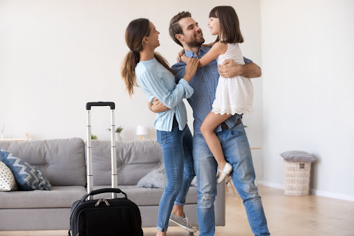 A man, woman, and young girl in a living room with a suitcase.