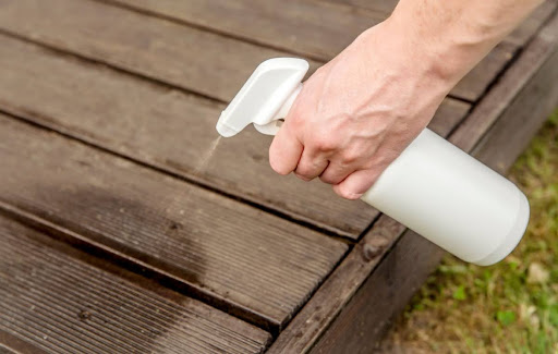 A hand spraying an insect repellent on a deck.