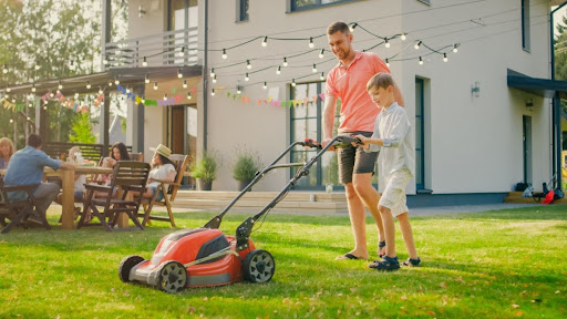A father and son mowing the grass in a backyard.