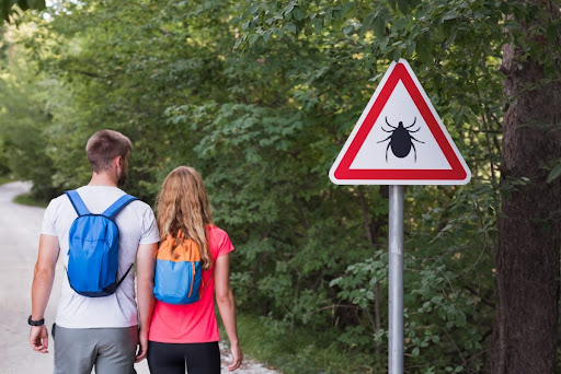 A man and a woman walking on a trail and passing a warning sign with a tick on it.
