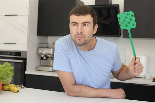 A man holding a fly swatter in a kitchen.