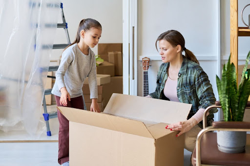 A woman and her daughter opening a cardboard box in a home.