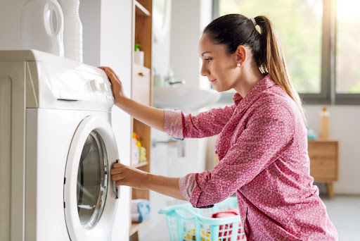 A woman using a washing machine in a home laundry room.